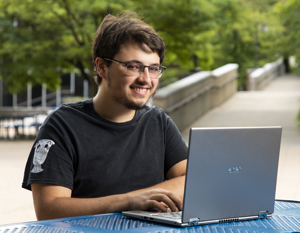 Photo of student working on a laptop outside on campus