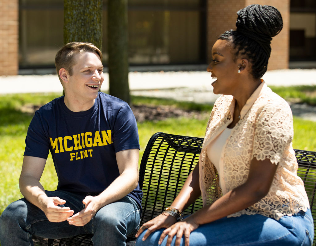 Two students sitting on bench outside.