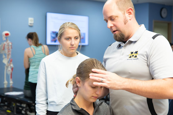 Faculty member working with two students in Physical Therapy class.