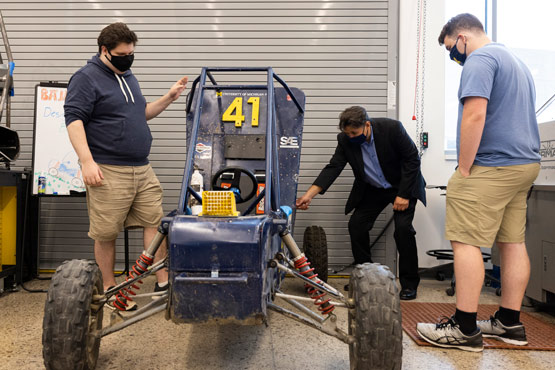 Two students and a professor woking on the University of Michigan-Flint Baja car.