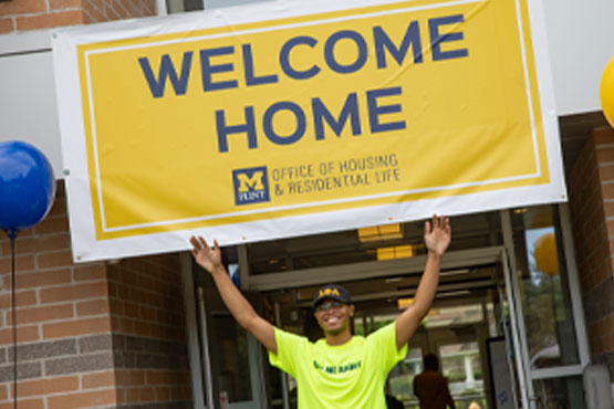 ساكن يحمل لافتة ترحيب بيت عند مدخل First Street Residence Hall في UM-Flint.