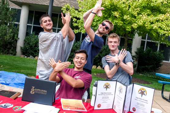 Four UM-Flint fraternity members sitting at a table outside the University Center.