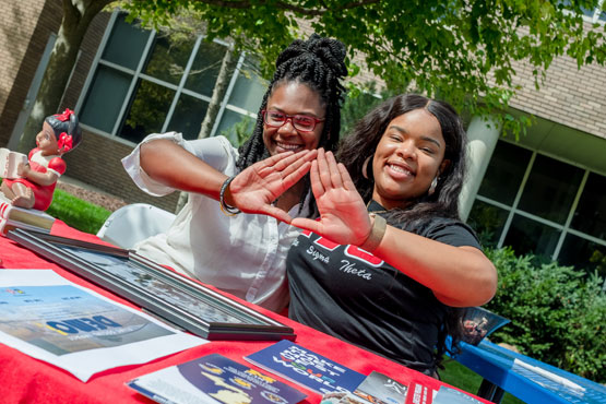 Two UM-Flint sorority members sitting at a table smiling.
